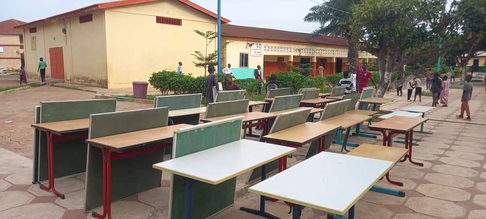 Schulmöbel stehen zur Übergabe auf einem Schulhof in Guinea bereit